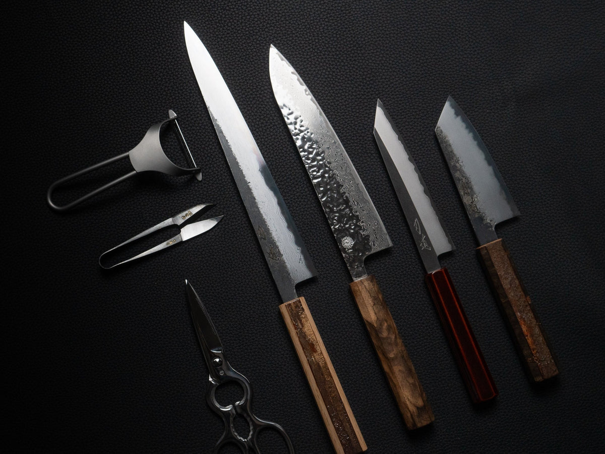 Fire japanske kniver med smiehud, damaskusmønster og blanke egger på svart underlag, med skrellekniv og saks