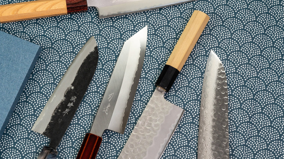 Fire japanske kniver, blant dem en med mørk smiehud, på blått tøy med bølgemønster