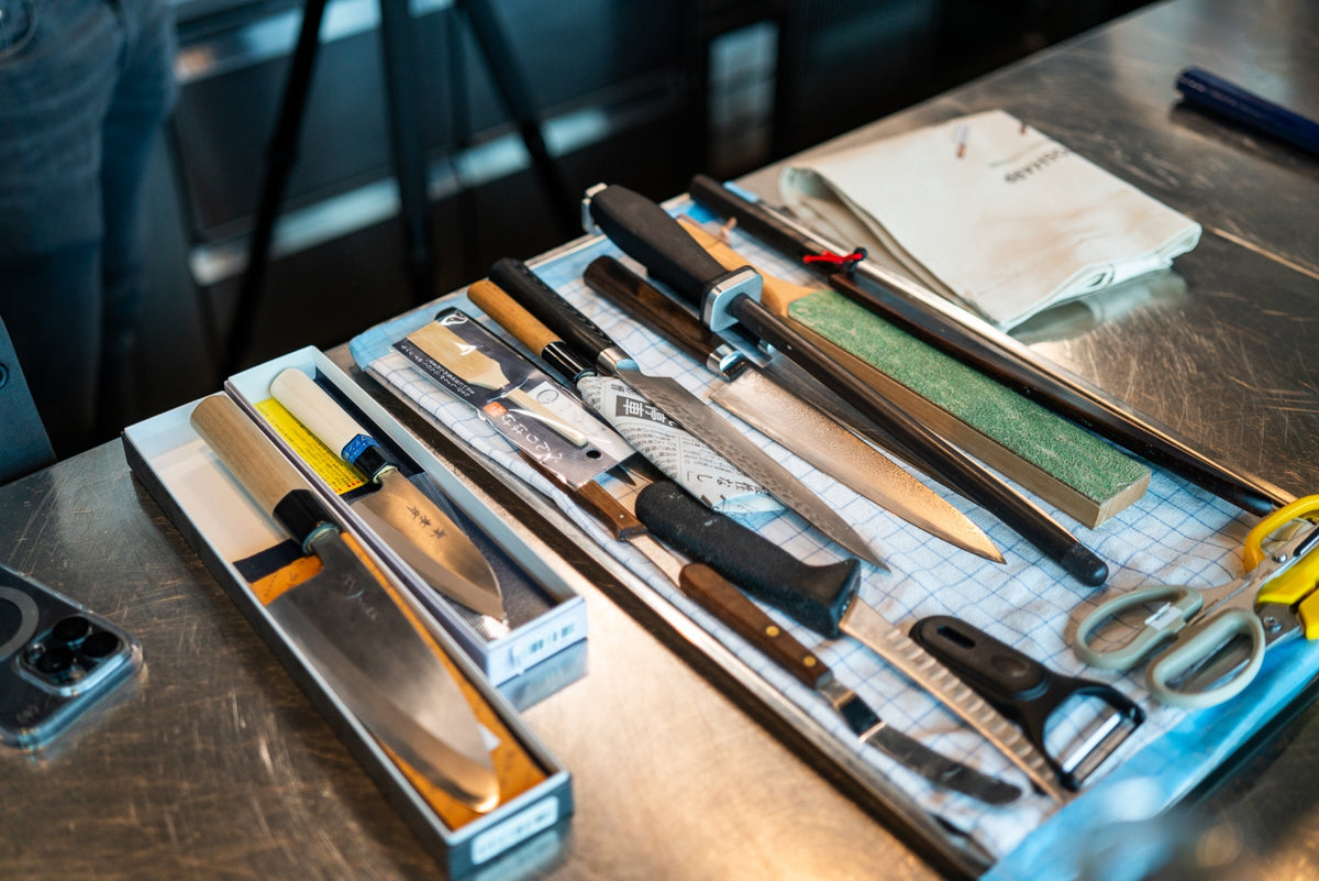 Kokkens kniver, slipestein og knivrull på en stålbenk i et restaurantkjøkken