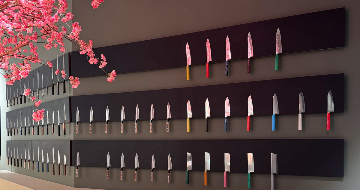 Knivveggen i butikken i Teknostallen med tre rader japanske kniver og kirsebærgrener