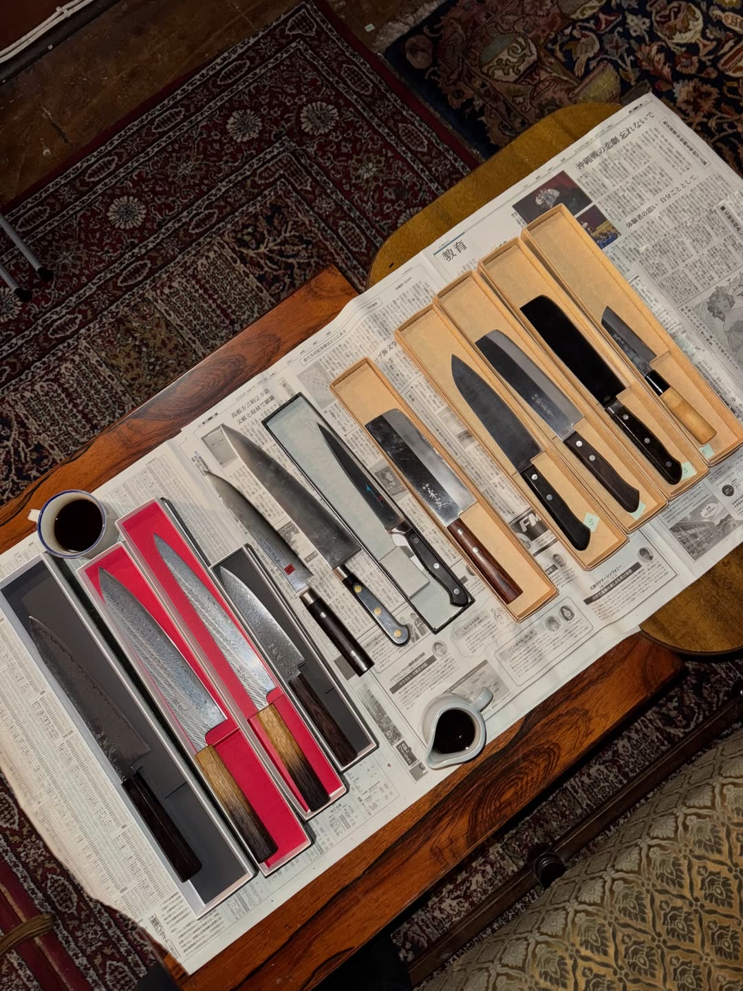 Vintage og brukte japanske kniver i hver sin eske på japansk avispapir, på et bord med persisk teppe og en kaffekopp