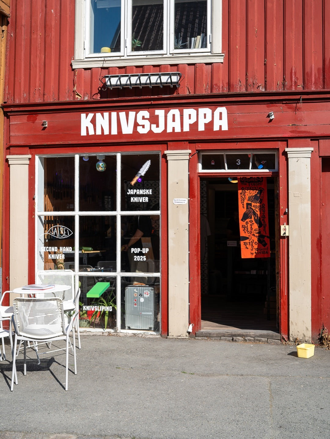 Rød trebygård i Nedre Bakklandet 3 med skiltet KNIVSJAPPA over døra og hvite kafestoler utenfor