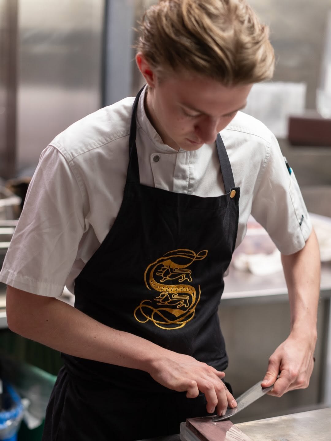 Kokk sliper en kniv på slipestein i et restaurantkjøkken