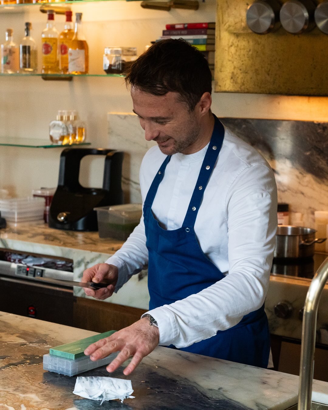 Kokk i forkle sliper kniv på våtstein i restaurantkjøkkenet