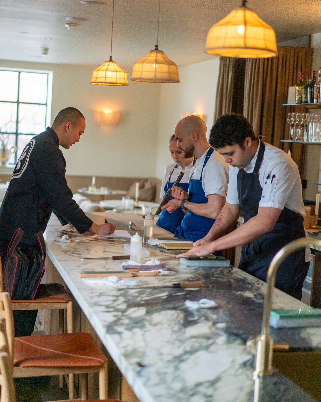 Kokker sliper kniver ved marmorbenken under slipedemonstrasjon i restauranten